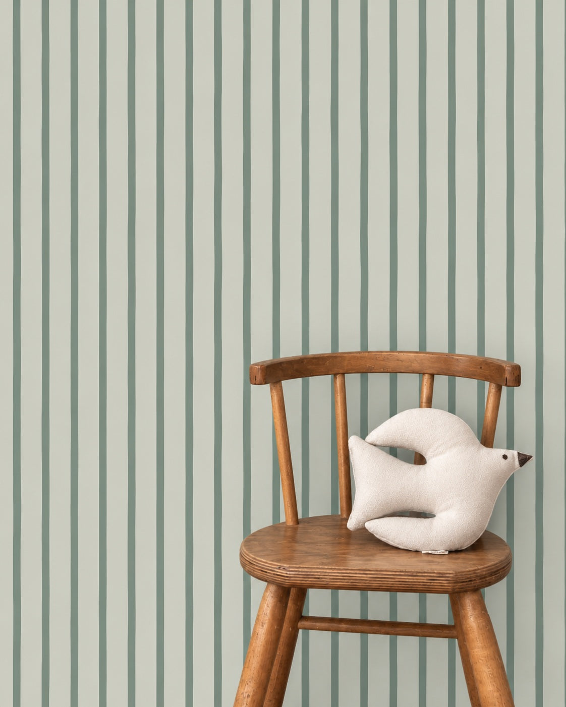 Flow Stripes - cloudy sage behang als achtergrond bij een houten stoel met een wit vogelkussen