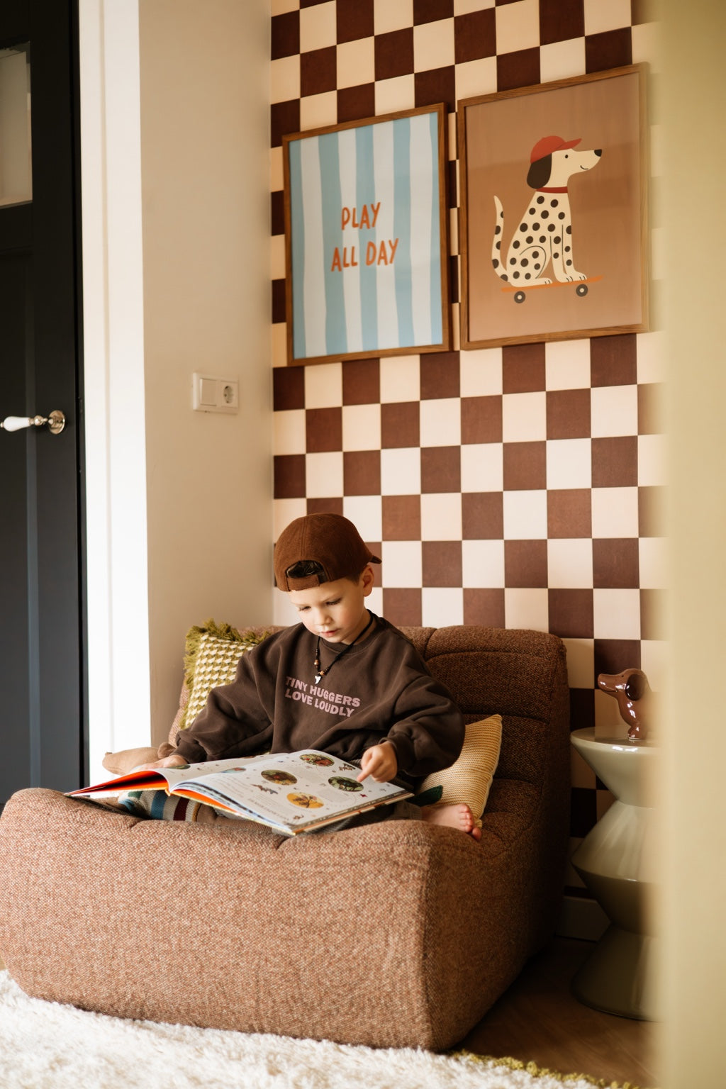 Kind leest in een bruine stoel onder Play all Day en Skater Dalmatier met Pet, met bruin-crème geblokt behang