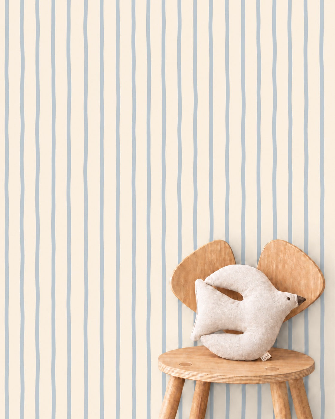 Flow Stripes - vanilla blue behang als achtergrond bij een houten stoel met een wit vogelkussen